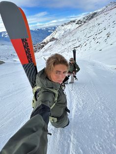 a woman holding skis in her hand on the side of a snow covered mountain