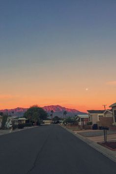 the sun is setting on an empty street with houses in the background and mountains in the distance