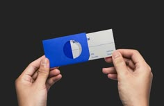 two hands holding up a blue and white business card with the letter d on it