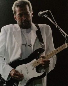 a man playing an electric guitar while standing in front of a microphone and holding it