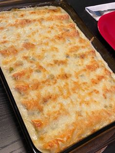 a casserole dish with cheese and vegetables in it sitting on a table next to a red plate