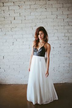 a woman standing in front of a brick wall wearing a white and black wedding dress