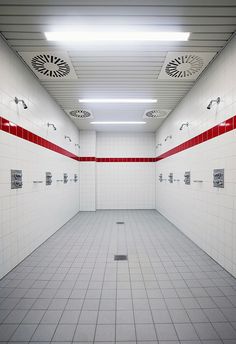 an empty public bathroom with red and white tiles on the walls, shower heads, and floor