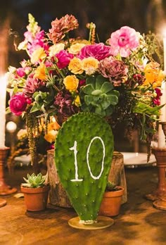 a table topped with a cactus plant and lots of flowers next to two lit candles