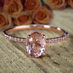 an oval shaped morganite and diamond ring on a table with roses in the background