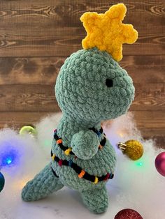 a crocheted stuffed animal with a crown on its head sitting in front of christmas ornaments