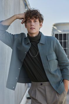 a young man is leaning against a wall with his hands on his head and looking at the camera