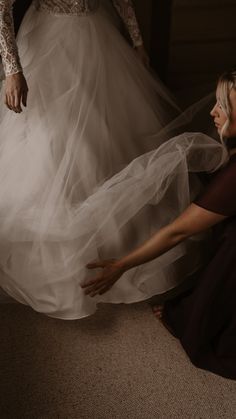 two women in wedding dresses are touching each other's hands while they stand on the floor