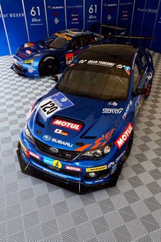 two racing cars are parked next to each other on a checkered floor in front of a blue wall