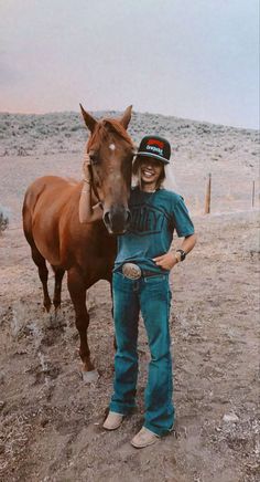 a woman standing next to a brown horse on top of a dry grass covered field