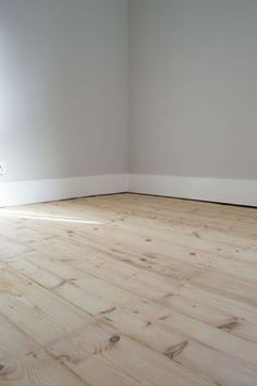 an empty room with white walls and wood flooring is seen in this image from the corner