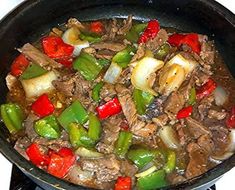 a skillet filled with meat and vegetables on top of a stove