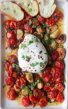 a white plate topped with bread and tomatoes on top of a bed of sauced cheese