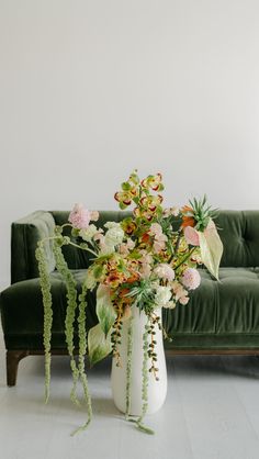 a white vase filled with lots of flowers on top of a table next to a green couch