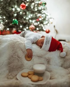 a baby in a santa hat sleeping on a blanket next to cookies