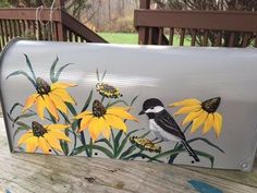 a painted mailbox sitting on top of a wooden table next to yellow flowers and butterflies