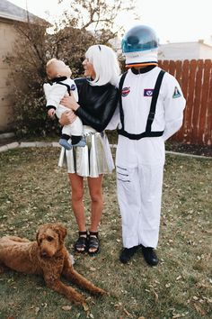 a man and woman in space suits holding a baby while standing next to a dog