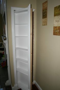 an empty white refrigerator in the corner of a room next to a wall with pictures on it