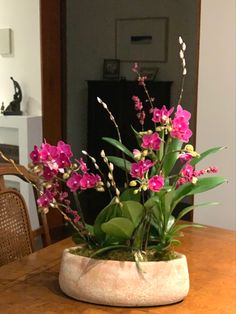 a wooden table topped with a vase filled with pink flowers and greenery next to a fire place