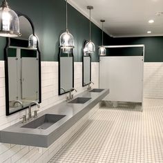 a public restroom with three sinks and two mirrors on the wall, lights hanging above them