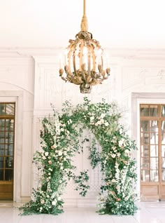 a chandelier hanging from the ceiling in front of a white room with flowers and greenery