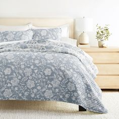 a bed with a blue and white comforter on it in a bedroom next to a dresser