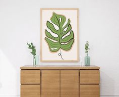 a large green leaf is hanging on the wall above a dresser