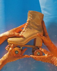 two hands hold up an orange pair of roller skates in front of a blue background