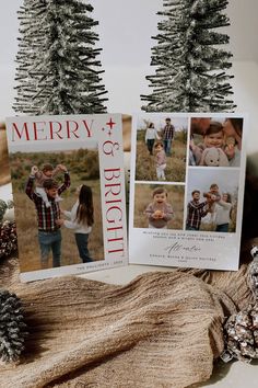 two christmas cards sitting on top of a table next to pine cones and fir trees