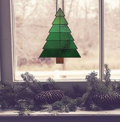 a stained glass christmas tree hanging from a window sill with pine cones on the windowsill