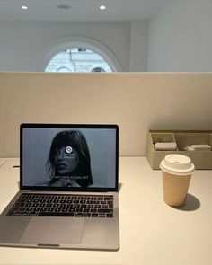 an open laptop computer sitting on top of a white desk next to a cup of coffee