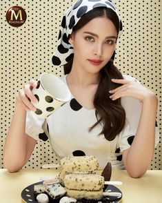 a woman is sitting at a table holding a cup and plate with cookies on it