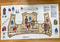 a piece of cloth with houses and birds on it sitting on a wooden floor next to a ruler