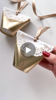 a person is holding two gold and white paper bells with lace on them, one has a video play button in the middle