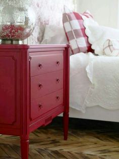 a red chest of drawers sitting in front of a bed with white sheets and pillows