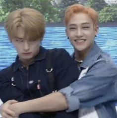 two young men sitting next to each other in front of a blue wall and water