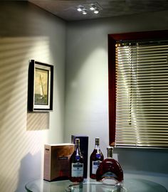 two bottles of liquor sit on a glass table in front of a window with blinds