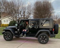 a woman sitting in the driver's seat of a black jeep parked on a driveway