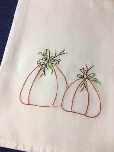 two embroidered pumpkins sitting on top of a white napkin with orange thread and green leaves