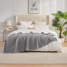 a bed with a blanket and pillows on top of it in a bedroom next to a potted plant