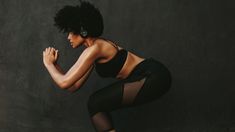 a woman with black hair and headphones is squatting on one leg, her hands in the air