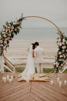 a bride and groom standing in front of an arch with candles on the beach behind them