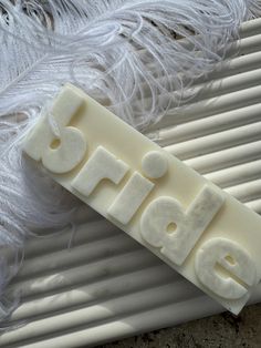 the word bride spelled out in white plastic letters on a piece of paper next to some feathers