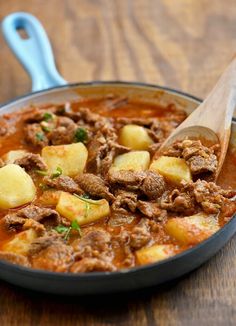 a wooden spoon is in a bowl of stew with potatoes and meats on the table