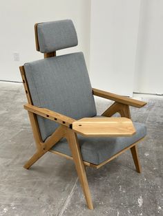 a chair with a wooden frame and arm rests on the floor in front of a white wall