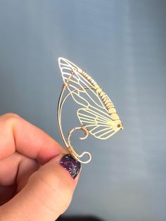 a hand holding a gold butterfly brooch with purple crystals on it's wings