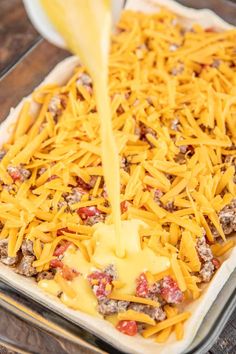 cheese being poured onto a casserole dish with ground beef and other toppings