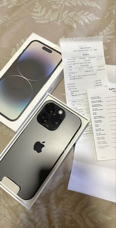 an apple phone in its box next to some papers on a bed with a receipt