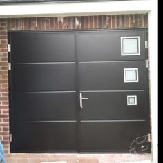 a black garage door with three windows on the side of it and a brick wall behind it