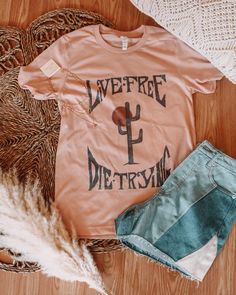 "Slip on our Live Free Soft Pink Graphic Tee, a western-style tee with a hand-drawn design featuring a punchy one-of-a-kind font and dusty boho cactus design - because if 'live free or die trying' isn't your motto, what is? Get ready to kick up some dust and make a statement in this sassy and stylish tee! Printed on Unisex Bella Canvas Crew Neck Tee. All orders are printed in the order in which they are received and arrive in an average of 7 days ---- ABOUT OUR PRINTING METHOD:  Lane Co. prints our tees Direct to Garment. The ink is applied directly into the fibers of the garment and will last a lifetime without ever peeling or cracking.  ---- CARE INSTRUCTIONS:  For the longest lifespan for your Lane Co. tees, we recommend washing your tees on cold and hanging them to dry. HOWEVER, I am s Free-spirited Cotton Crew Neck T-shirt, Free-spirited Cotton T-shirt With Graphic Print, Bohemian Graphic Print Tops For Streetwear, Clothing Flatlays, Punchy Style, Western Tshirt, Pink Graphic Tee, Boho Cactus, Cactus Tshirt